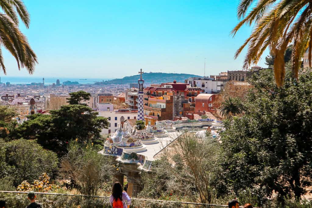 Overlooking Barcelona, the view from Park Güell showcases mosaic details, undulating benches, and the cityscape stretching to the sea under a sunny sky