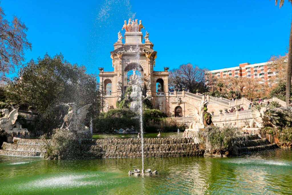 The Cascada Fountain in Barcelona's Parc de la Ciutadella, with water gushing and statues adorning it, set against a backdrop of trees and blue sky