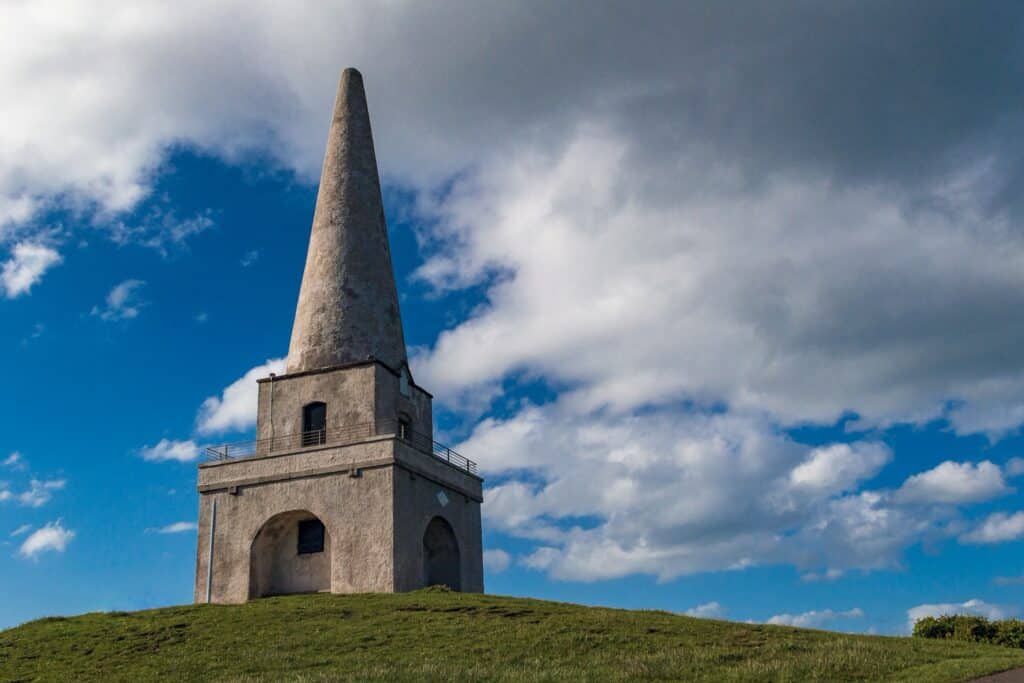 The historical Killiney Hill Obelisk standing tall against a bright blue sky with scattered clouds