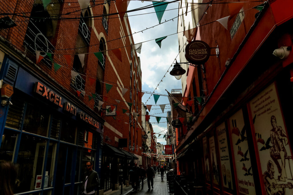 Dimly lit Temple Bar area in Dublin, adorned with flags and festive string lights, bustling with people