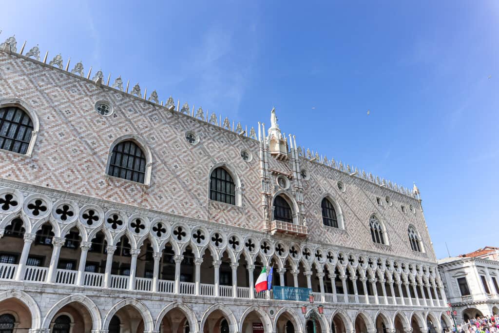 The Doge's Palace in Venice, with its patterned brick walls and ornate Gothic windows, stands proudly by the waterfront, reflecting the city's historical grandeur.