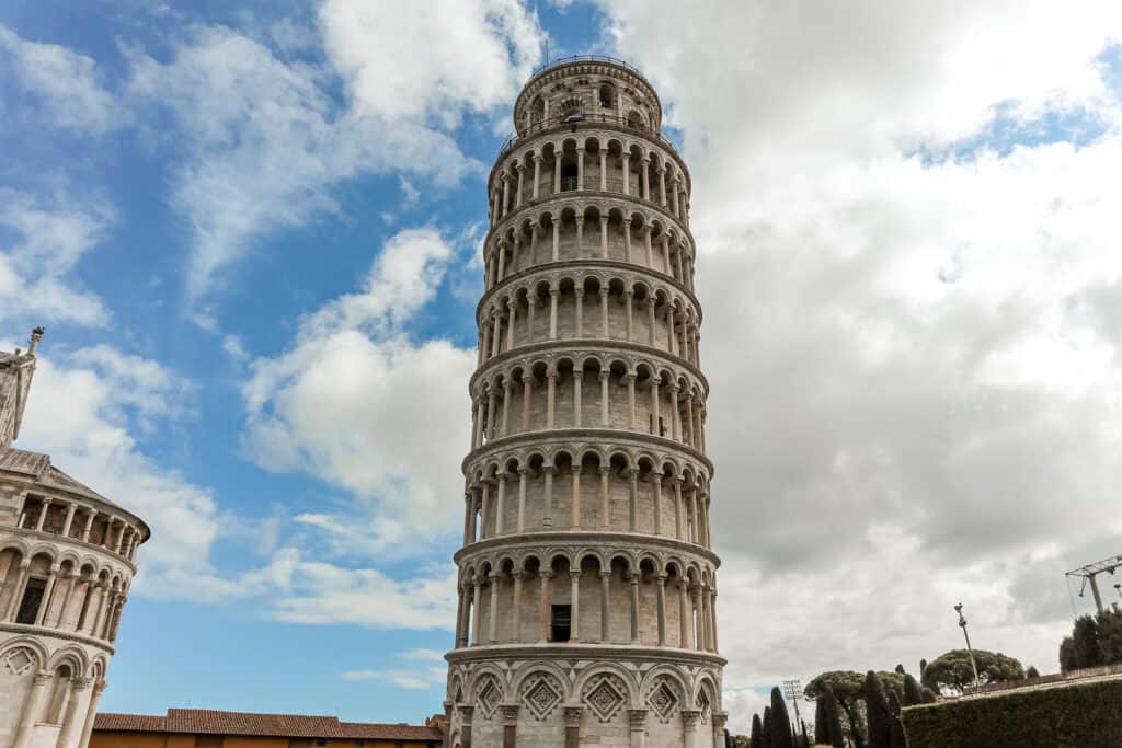 The Leaning Tower of Pisa rises against a partly cloudy sky, showcasing its iconic tilt and the intricate marble sculptures of its exterior.