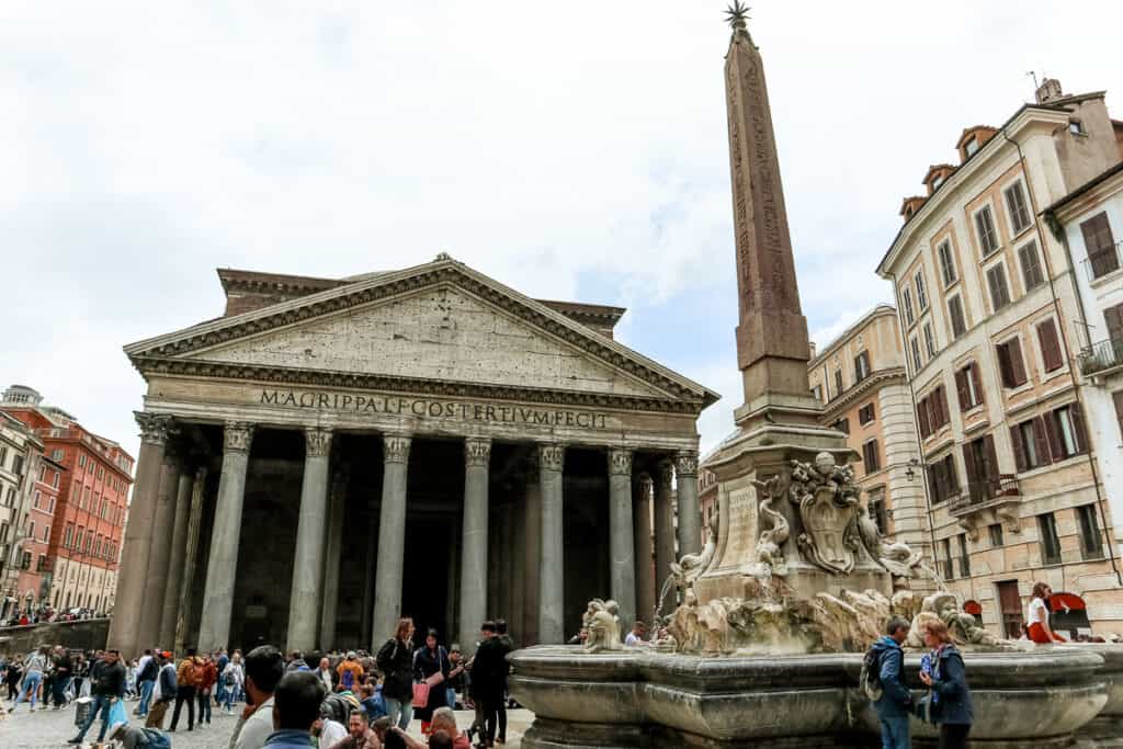 The Pantheon in Rome, an ancient architectural marvel, stands with its grand columns and pediment, bustling with tourists in the foreground.