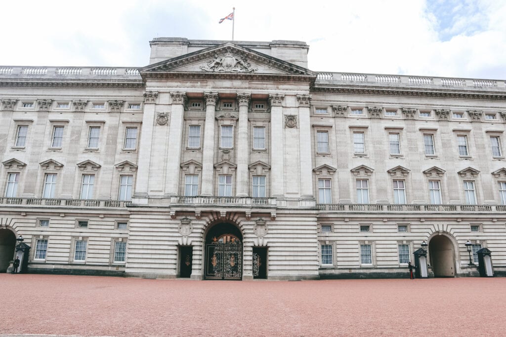 Buckingham Palace, the iconic residence of the British monarchy, presents its imposing facade and grand central balcony under a grey sky.