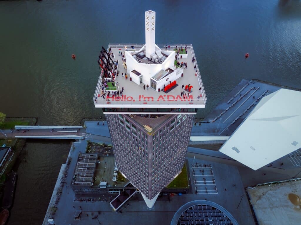 Aerial view of the A'DAM Lookout observation deck with the 'Hello, I'm A'DAM' greeting and visitors enjoying panoramic city views