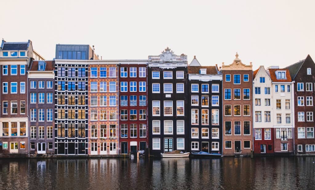 Iconic Amsterdam architecture with a row of colorful, narrow houses reflected in the calm canal waters at dusk