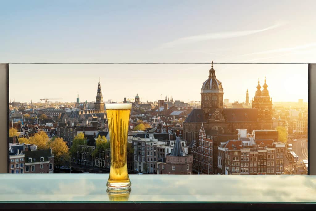 A close-up of a chilled beer glass with Amsterdam's iconic skyline in the background, capturing the essence of the city at sunset