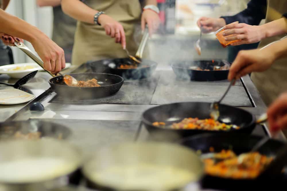 An engaging cooking class in action with multiple chefs sautéing dishes in pans over a stove, creating a dynamic culinary atmosphere.